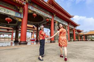 Rear view of Asian woman and her senior mother in red cheongsam qipao dress is visiting the Chinese Buddhist temple together during lunar new year for traditional culture concept photo