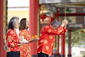 Asian family with senior parent in red cheongsam qipao dress is offering food to the ancestral god inside Chinese Buddhist temple during lunar new year for best wish blessing and good luck photo