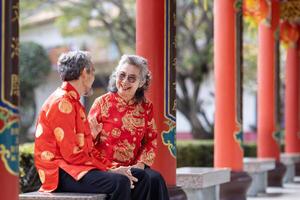 asiático matrimonio mayor Pareja en cheongsam qipao vestir es hablando a cada otro dentro el templo durante chino nuevo año para familia y relativo reunión en pueblo natal concepto foto