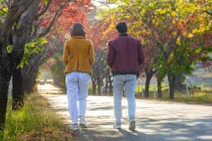 Happy caucasian couple are walking together in public park countryside road during autumn with maple and beech tree for fall color travel destination and partner happiness concept photo
