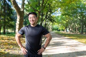 retrato de asiático atleta en otoño parque en soleado día, hombre en ropa de deporte sonriente y mirando a cámara, aptitud instructor antes de capacitación. foto