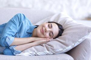 Close up photo portrait of young beautiful woman sleeping on sofa smiling through sleep, tired daytime sleep