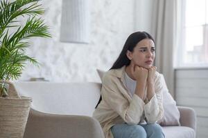 A sad and disappointed woman is alone at home sitting on the couch in depression, thinking. photo