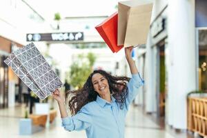 Happy shopper woman looking at camera and smiling, hispanic woman with curly hair dancing and jumping with pleasure, bought gifts on sale, portrait of happy shopping woman. photo