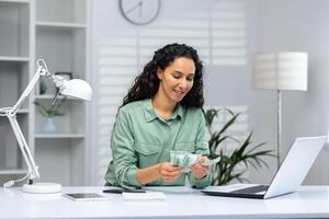 Joyful and successful businesswoman at workplace inside home office counting income arrived money american dollars cash. photo