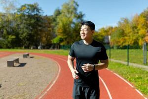 Young successful asian man jogging at daytime in stadium, man running and doing fitness active exercise in sports suit, active lifestyle. photo