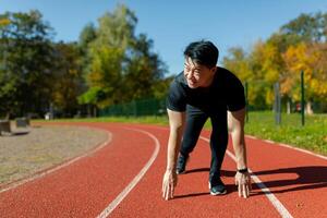 A young Asian man is an athlete, a runner. He is preparing for the start of the marathon, a race on the stadium's running track. photo