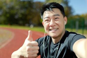 Asian young man talking in headphones on the news ringer at the stadium. Smiling and pointing at the camera with a super finger. Close-up photo. photo