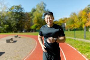 Portrait of a young Asian sportsman runner in black sportswear running in the stadium and smiling at the camera. photo