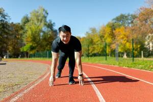 retrato de un joven asiático masculino atleta en pie en un estadio en un corriendo pista y preparando para el comienzo de un carrera. foto