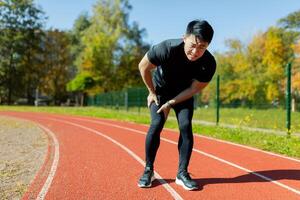 A runner injured his leg on a run in the afternoon, an Asian man has severe muscle spasm and pain in his leg during fitness and active exercise, a man in a tracksuit injured himself. photo