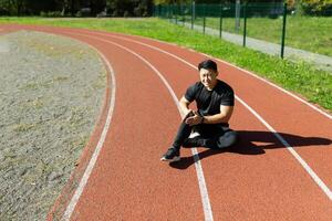 Sports injury. A young Asian man is sitting at the stadium on a treadmill, holding his leg and knee. He writhes in pain. Needs medical help. photo