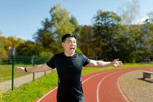 un joven asiático hombre es corriendo un maratón en el estadio, tomando parte en el competencia. carreras a el terminar línea y es contento con el resultado. foto