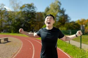 Satisfied and happy runner asian finish run, happy with good result reaching finish line, man in sportswear running in stadium. photo