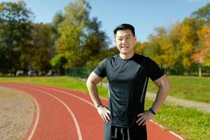 Portrait of a fitness instructor and trainer at a stadium in the afternoon on the grass, an Asian man smiling and looking friendly at the camera, a man in sportswear. photo