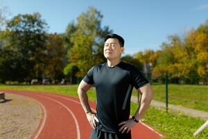 Portrait of a young Asian male athlete, trainer standing on a stadium treadmill. He closes his eyes, rests, breathes. Preparing for exercises, running. photo