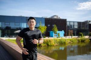 Happy Asian man running and exercising in the park, outdoors by the lake. Young athlete, outdoor runner and motivation for fitness, energy and healthy exercise. photo