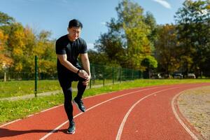 An Asian athlete injured his leg while running during training, a man injured himself at the stadium on a sunny day, stands tall and massages a muscle spasm on his leg. photo