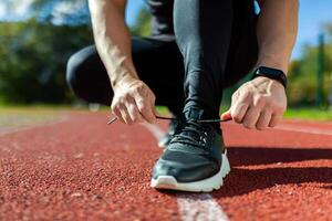 de cerca foto de un del hombre mano atadura cordones de los zapatos a un Deportes estadio, un corredor antes de comenzando un correr y capacitación, en un soleado día.