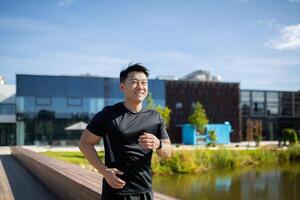 Asian smiling young man dressed in sportswear is doing a morning jog in the park near the lake. photo