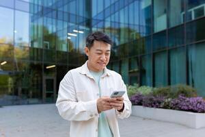 A young male Asian student is standing in a dormitory near the campus and using the phone. photo