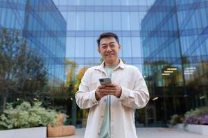 Portrait of a smiling young businessman standing in front of an office building and using the phone. photo