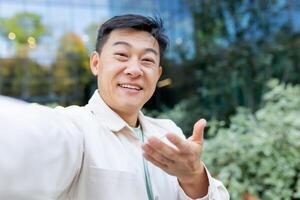 Close-up photo. A young male Asian student is standing outside the campus and talking on a call. Takes selfies, records on , podcast, blogger. photo