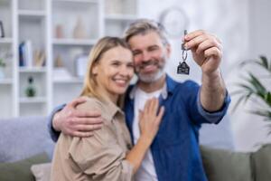 Selected focus, senior gray-haired couple, man and woman hugging together in new apartment house, happy family holding house keys. photo