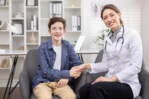 Happy teenager boy patient and female doctor shaking hands, successful reception consultation in bright office of private clinic, health concept, doctor professional, smiling looking at camera. photo