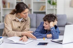 A female tutor works with a boy student in a bright living room at home, schoolboy is tired and dissatisfied with his studies, leans on his hand, does not listen his mother, who helps with homework. photo