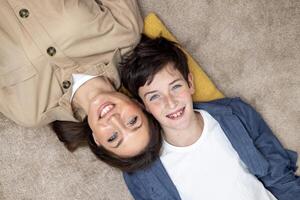 Portrait of happy woman with son, mother and boyfriend smiling and looking at camera lying together on carpets on floor at home in living room, having fun together. photo