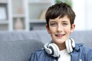 Close-up portrait of young schoolboy boy at home, teenager smiling and looking at camera in living room, wearing headphones. photo
