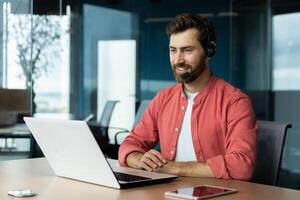 Happy customer service worker with call headset and laptop, man smiling and consulting customers online helps place order photo