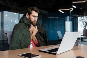 Office worker is freezing at work, there is no heating and broken office heating, businessman is working with a laptop, I will put on outerwear. photo