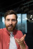 Close-up photo. Young businessman, freelancer, programmer conducts a conference on a call, holds a phone in his hands, talks to the camera, vertical photo. photo