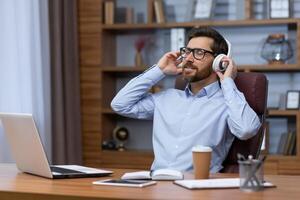 Rest, break at work. A young businessman sitting in the office, leaning on a chair, listening to music in headphones, closed his eyes, relaxed. photo