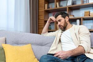 Sad mature man in depression sitting alone at home on sofa in living room. photo