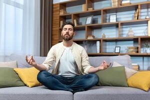 Mature man alone at home resting after work sitting in lotus position on sofa in living room meditating and relaxing. photo