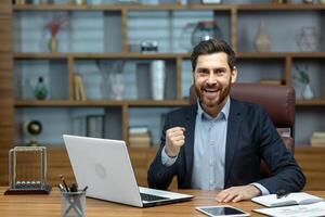 Portrait of mature senior businessman in office, man looking at camera and holding hands up super power and superhero gesture, successful investor using laptop inside building. photo