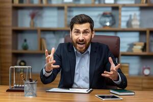 Angry and screaming businessman inside office talking on call, boss shouting in online meeting with colleagues and subordinates, dissatisfied with work of colleagues and partners. photo