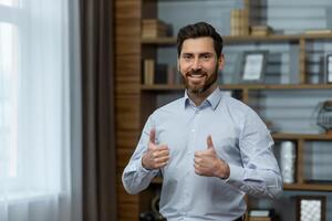 Successful businessman smiling and looking at camera, man shows thumbs up affirmatively and joyfully agrees with achievement, boss in shirt inside office at work. photo