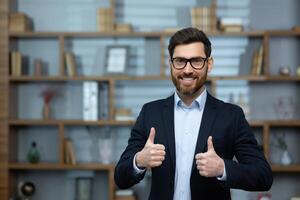 Portrait of a successful financier inside the office, the man is smiling and looking at the camera, showing a positive thumbs up, photo