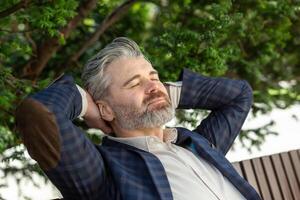 mayor profesional hombre en negocio atuendo toma un pacífico descanso al aire libre, reflejando con ojos cerrado en medio de verdor. foto