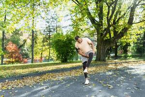 Runner injured his leg while jogging in the park near the trees, hispanic man has muscle spasm massaging his knee, man is running and exercising fitness on a sunny day. photo