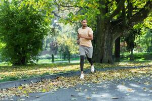 Hispanic man jogging in the park on a sunny day, runner listening to music in wired headphones, audio books and podcasts, sportsman happy with an active weekend. photo