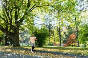 Hispanic man jogging in the park on a sunny day, runner listening to music in wired headphones, audio books and podcasts, sportsman happy with an active weekend. photo