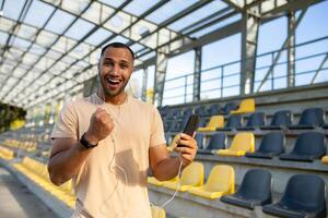 A successful man, satisfied with the result of training, looks at the camera and smiles, Hispanic holds a phone in hands uses an online sports program, an athlete holds his hand up in achievement. photo