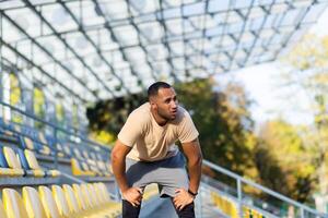 Tired hispanic athlete kneeling, standing in stadium and resting after running, exercising, training. photo