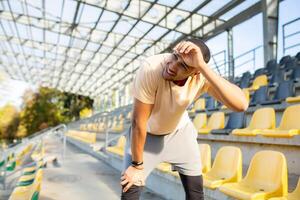 Tired hispanic athlete bent over and breathing after jogging, man doing sports on sunny day with active exercises and fitness, athlete resting after jogging. photo