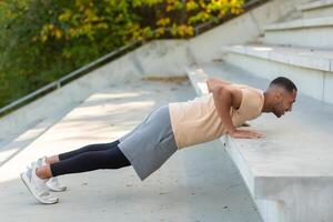 Cheerful and smiling hispanic man doing outdoor exercise in stadium, man stretching and recuperating before jogging in summer park. photo